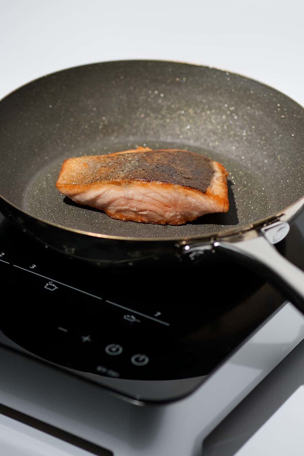 crispy salmon in diamond frying pan on a induction cooktop.