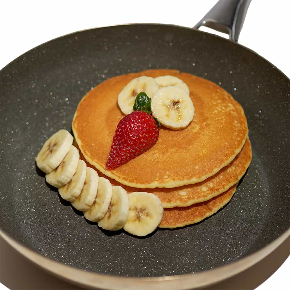 pancakes with banana slices and a strawberry in a sparkling diamond frying pan.