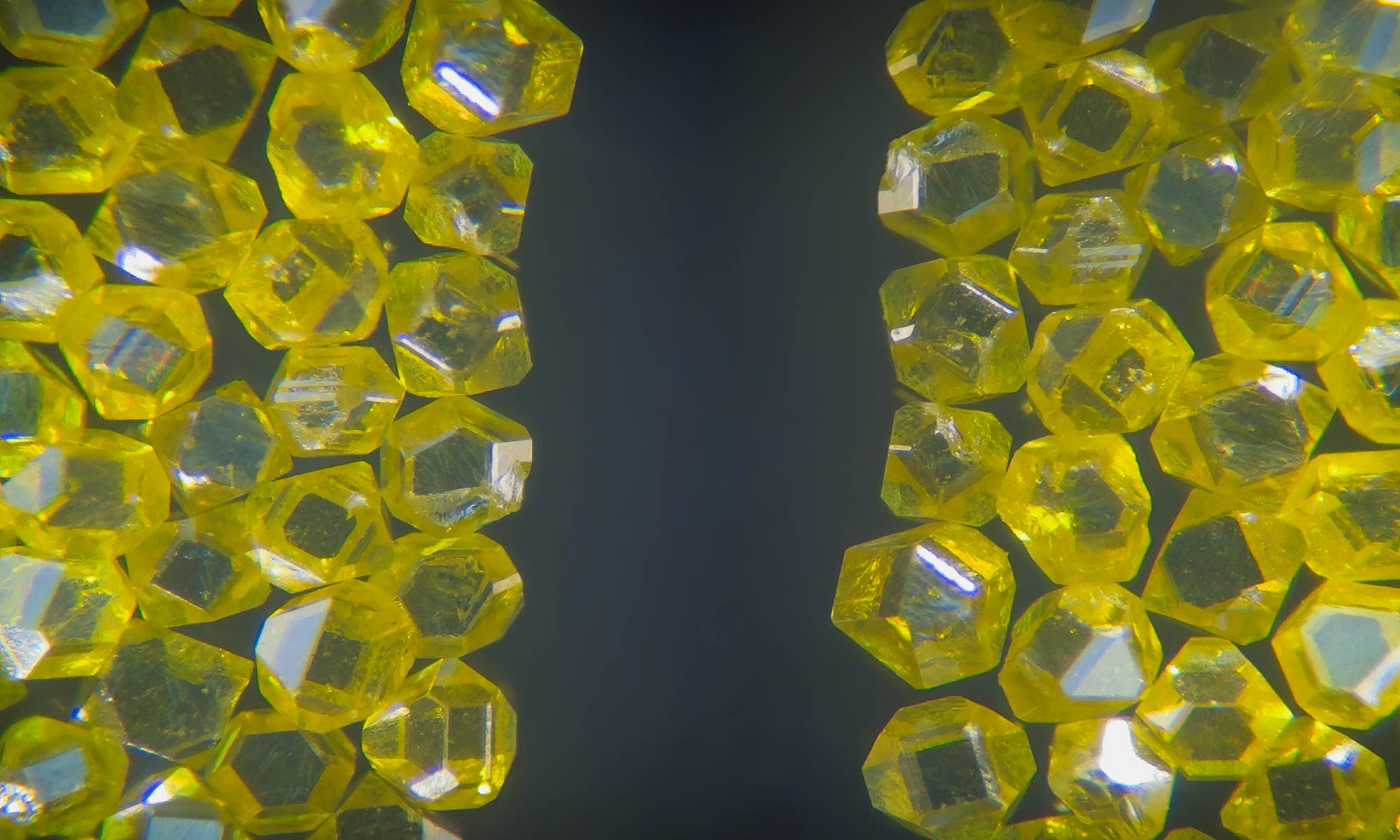 Macro view of raw, faceted yellow diamond crystals framing the left and right sides of a dark background.