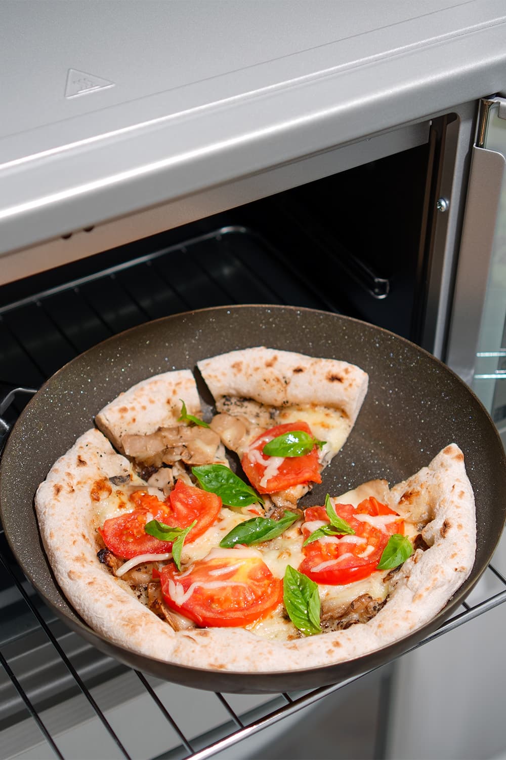 Pizza with tomatoes and basil baking in diamond skillet inside oven
